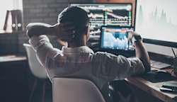 A man looking at many computer monitors filled with charts and graphs.